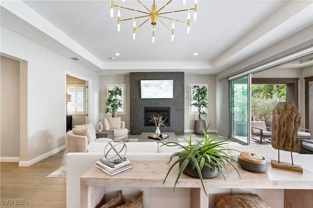 living room featuring a tray ceiling, a chandelier, a large fireplace, and light hardwood / wood-style floors