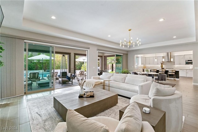 living room with light wood-type flooring, a tray ceiling, and a chandelier