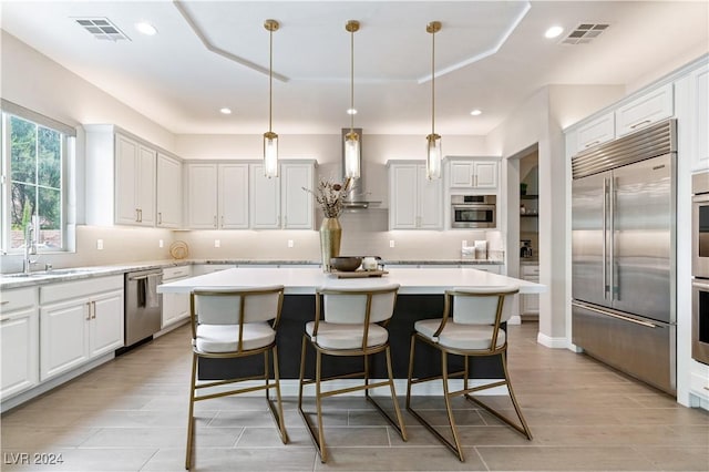 kitchen featuring white cabinets, appliances with stainless steel finishes, a kitchen island, and hanging light fixtures