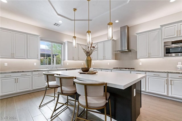 kitchen featuring white cabinetry, wall chimney range hood, light hardwood / wood-style flooring, pendant lighting, and a kitchen island