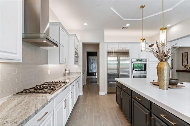 kitchen featuring pendant lighting, white cabinets, wall chimney range hood, and appliances with stainless steel finishes