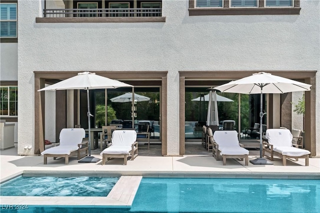 rear view of property featuring a swimming pool with hot tub, a balcony, and a patio