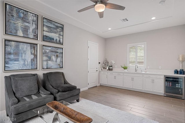 living room featuring ceiling fan, light hardwood / wood-style floors, sink, and wine cooler