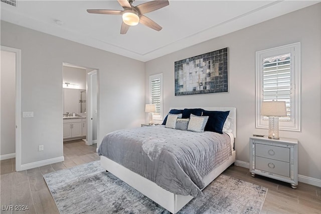 bedroom featuring ensuite bath, ceiling fan, multiple windows, and light wood-type flooring