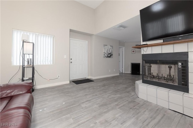 living room featuring a tiled fireplace, light wood-type flooring, and a high ceiling