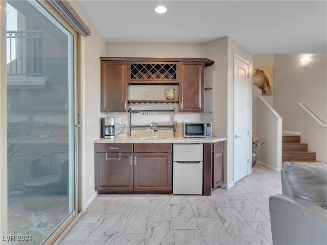 bar with dark brown cabinetry, white refrigerator, light stone counters, and sink