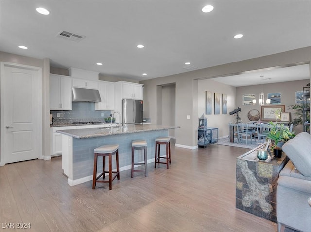 kitchen featuring light wood-type flooring, white cabinetry, stainless steel appliances, and an island with sink