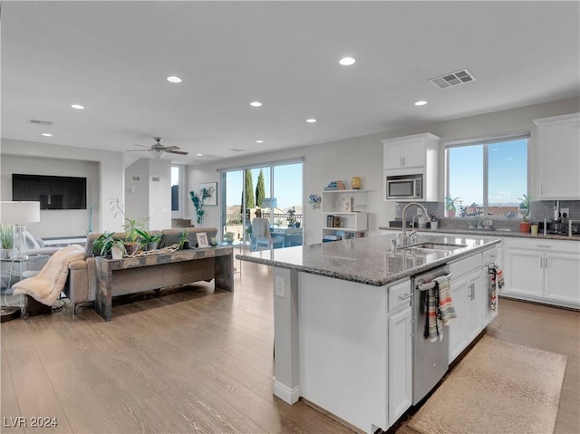 kitchen with stainless steel appliances, a kitchen island with sink, plenty of natural light, and dark stone countertops