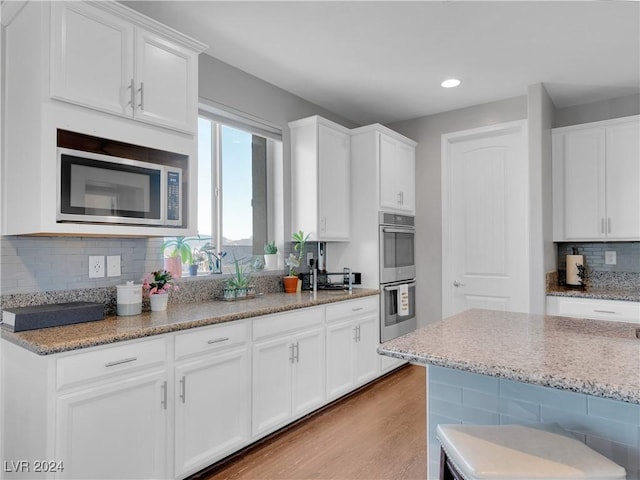 kitchen featuring appliances with stainless steel finishes, tasteful backsplash, light hardwood / wood-style floors, light stone counters, and white cabinetry