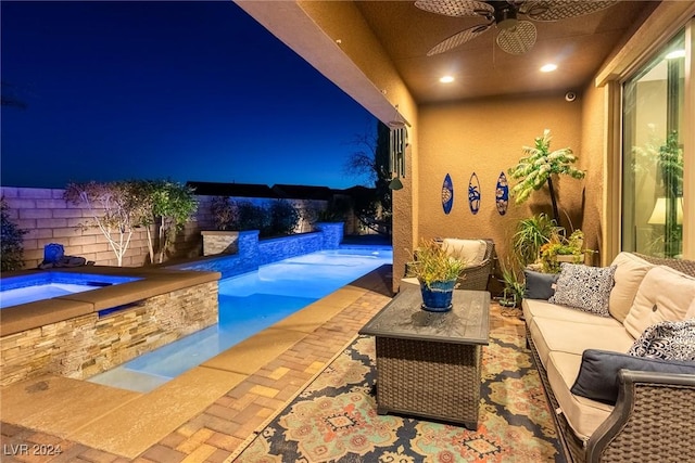 pool at night with outdoor lounge area, ceiling fan, and an in ground hot tub