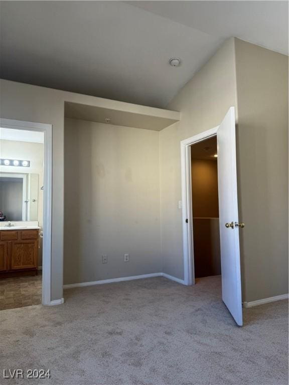 unfurnished bedroom with ensuite bathroom, lofted ceiling, and light colored carpet