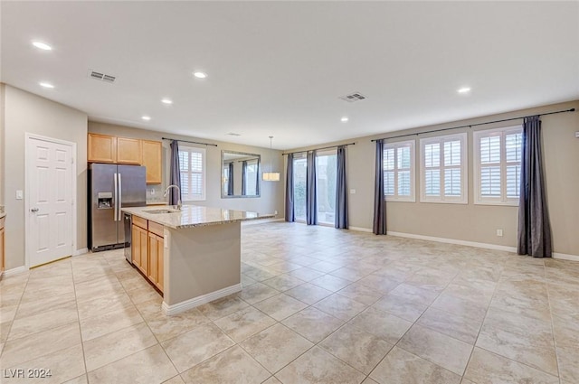 kitchen featuring light brown cabinetry, light stone counters, stainless steel appliances, sink, and an island with sink