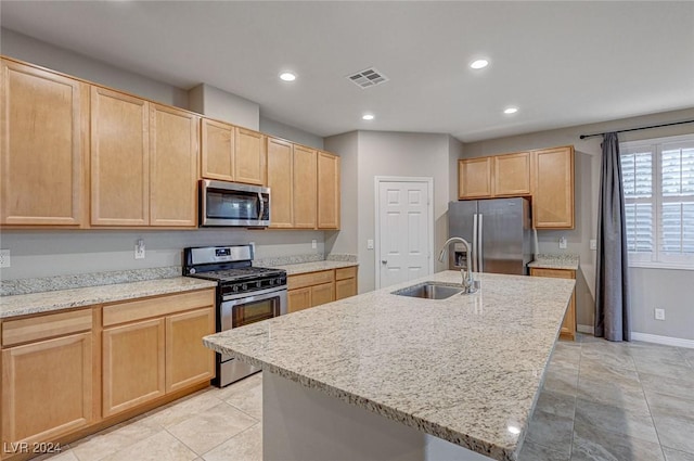 kitchen with sink, light stone countertops, stainless steel appliances, and an island with sink