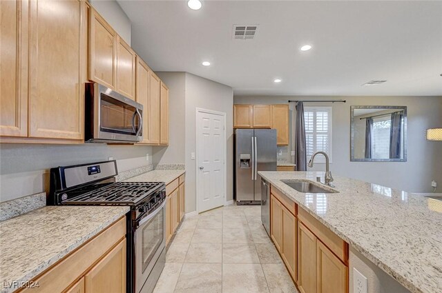 kitchen with light stone countertops, stainless steel appliances, sink, light brown cabinets, and light tile patterned floors