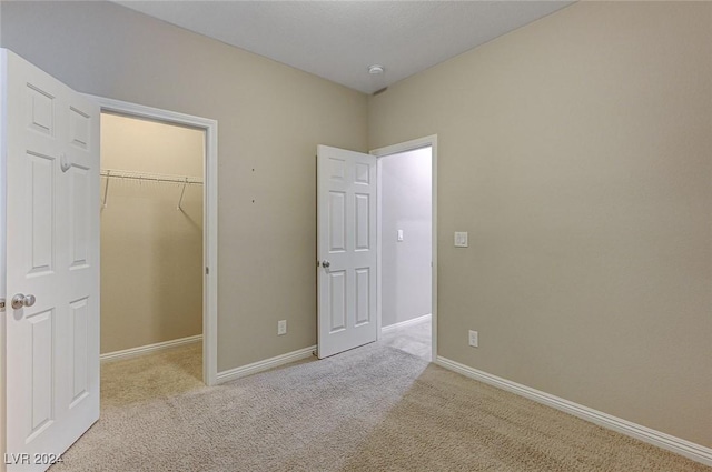 unfurnished bedroom featuring a spacious closet, light carpet, and a closet