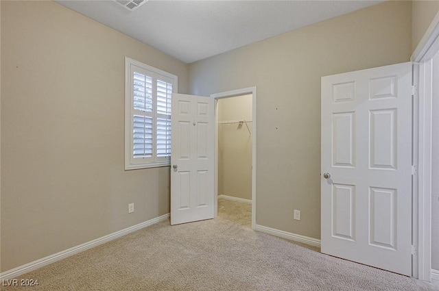 unfurnished bedroom featuring a walk in closet, light colored carpet, and a closet