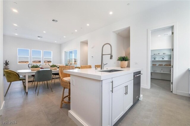 kitchen with a kitchen bar, white cabinetry, sink, and an island with sink