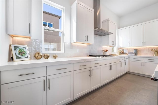 kitchen with decorative backsplash, light tile patterned flooring, white cabinetry, and wall chimney range hood