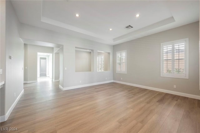 empty room featuring a tray ceiling and light hardwood / wood-style floors