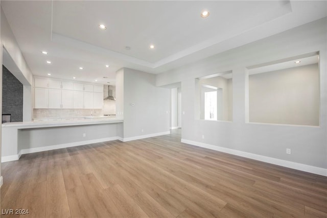 unfurnished living room with a tray ceiling, a fireplace, and light hardwood / wood-style floors