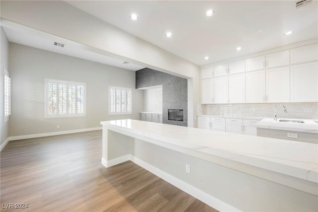 kitchen featuring light stone countertops, backsplash, sink, light hardwood / wood-style flooring, and white cabinetry