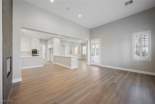 unfurnished living room featuring a fireplace, light hardwood / wood-style flooring, and a high ceiling