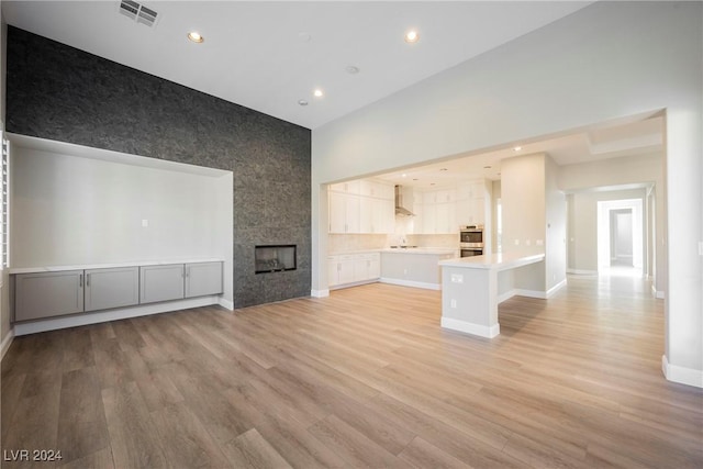 unfurnished living room with a tile fireplace, light hardwood / wood-style floors, and a high ceiling