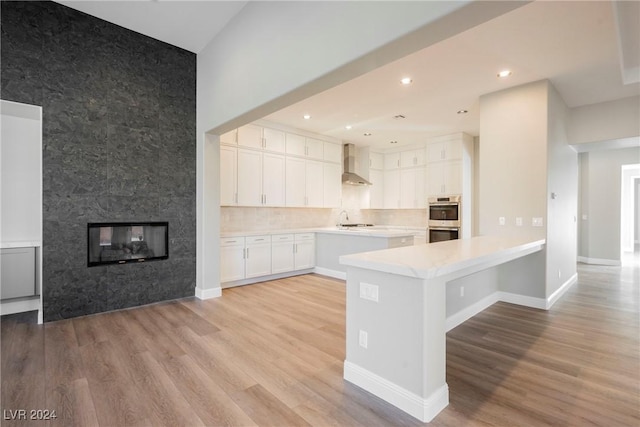 kitchen featuring wall chimney exhaust hood, stainless steel double oven, white cabinetry, and light hardwood / wood-style flooring