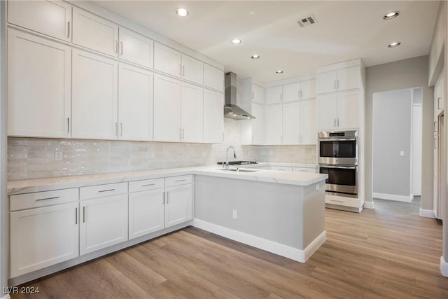 kitchen with white cabinets, decorative backsplash, stainless steel appliances, and wall chimney range hood