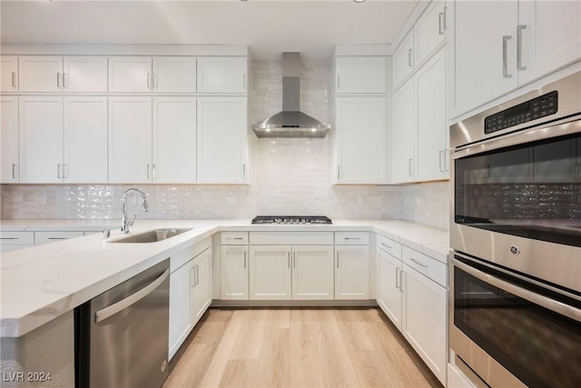 kitchen featuring appliances with stainless steel finishes, sink, white cabinetry, and wall chimney range hood