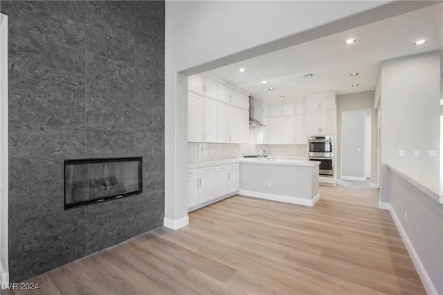 kitchen with white cabinetry, sink, wall chimney exhaust hood, light hardwood / wood-style flooring, and a tiled fireplace