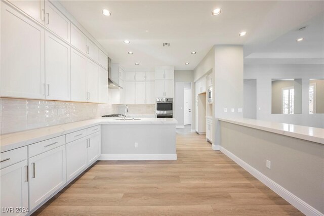 kitchen with wall chimney exhaust hood, decorative backsplash, white cabinets, and light hardwood / wood-style floors