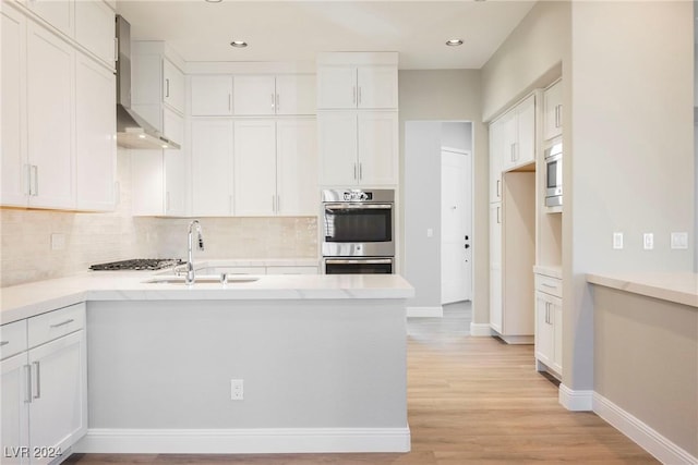 kitchen featuring white cabinetry, sink, wall chimney exhaust hood, light hardwood / wood-style floors, and appliances with stainless steel finishes