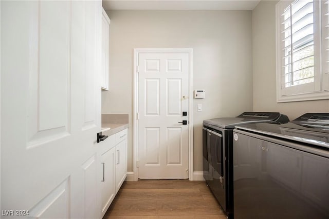 clothes washing area featuring cabinets, washing machine and dryer, and light hardwood / wood-style flooring