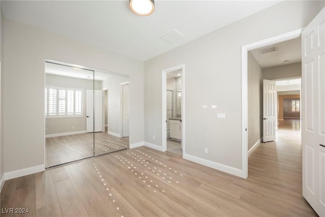 unfurnished bedroom featuring ensuite bathroom, a closet, and light hardwood / wood-style flooring