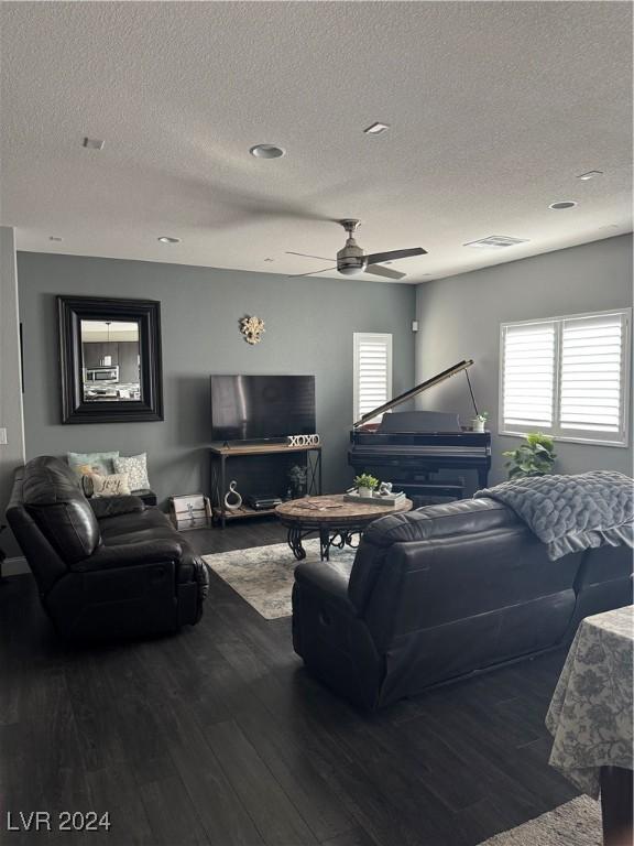 living room featuring ceiling fan, dark wood-type flooring, and a textured ceiling