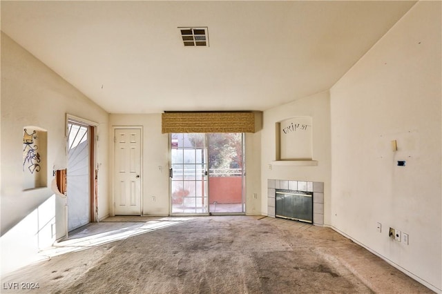 unfurnished living room with carpet flooring, plenty of natural light, vaulted ceiling, and a tiled fireplace