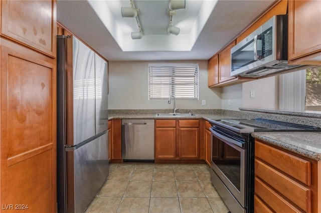 kitchen featuring sink, rail lighting, stainless steel appliances, a raised ceiling, and light tile patterned flooring