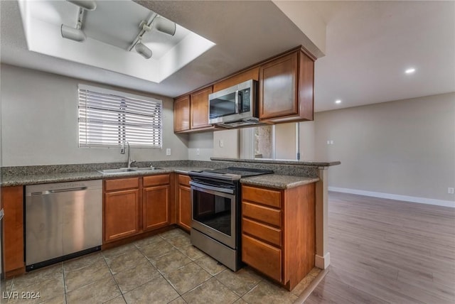 kitchen with sink, stainless steel appliances, kitchen peninsula, track lighting, and hardwood / wood-style flooring