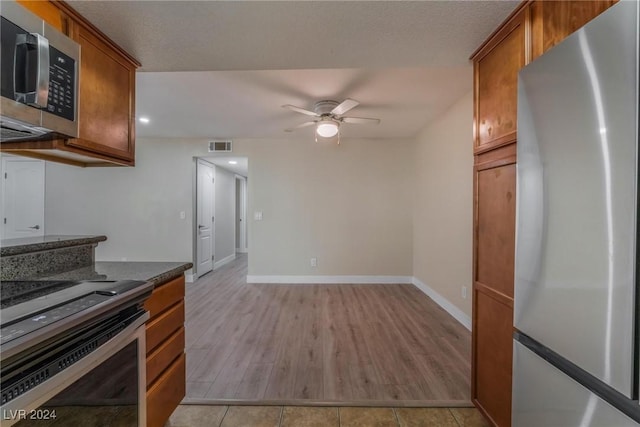 kitchen with dark stone counters, ceiling fan, stainless steel appliances, and light hardwood / wood-style floors