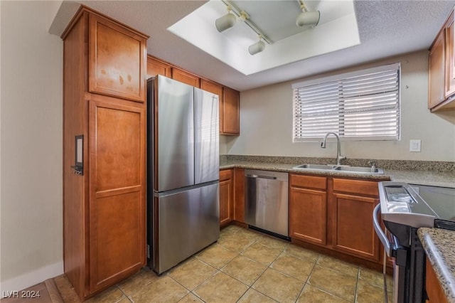 kitchen with appliances with stainless steel finishes, light tile patterned floors, a raised ceiling, and sink