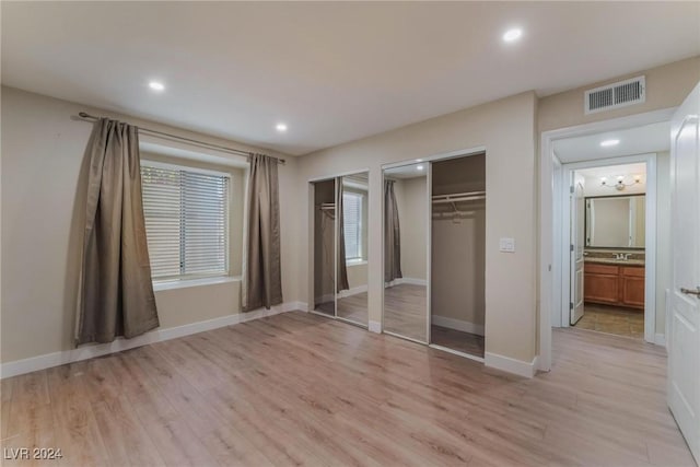 unfurnished bedroom with ensuite bath, light hardwood / wood-style flooring, two closets, and sink