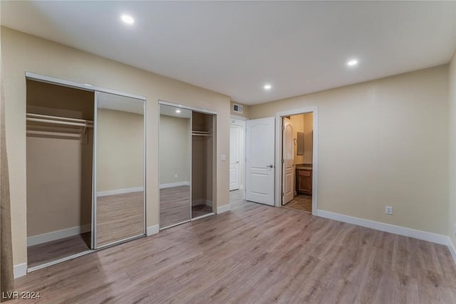 unfurnished bedroom featuring light wood-type flooring, two closets, and ensuite bath