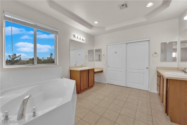 bathroom with a raised ceiling, vanity, tile patterned floors, and a tub to relax in