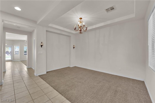 carpeted spare room featuring a raised ceiling and an inviting chandelier