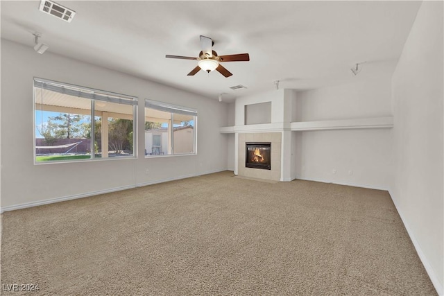 unfurnished living room with ceiling fan, carpet flooring, and a tiled fireplace