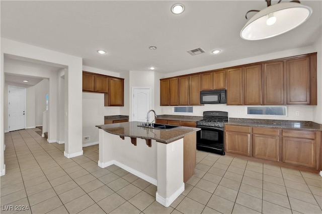 kitchen with sink, light tile patterned floors, black appliances, and an island with sink