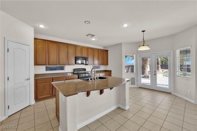 kitchen featuring sink, hanging light fixtures, light tile patterned floors, stainless steel range with gas cooktop, and a kitchen island with sink