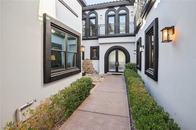 view of exterior entry featuring a balcony, french doors, and stucco siding