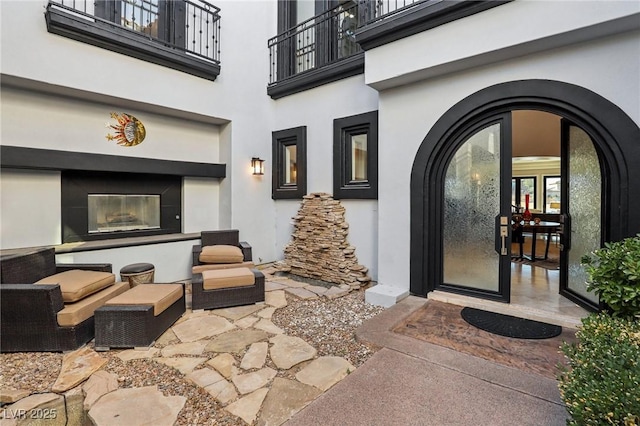 property entrance with a glass covered fireplace, stucco siding, a patio, and a balcony